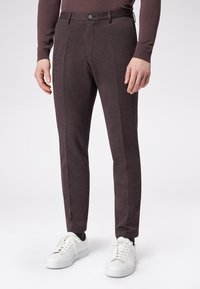 Ciemnobrązowe dopasowane spodnie w fakturowanej tkaninie, z gładkim przodem, szlufkami na pasek i zwężanymi nogawkami, zestawione z białymi trampkami.