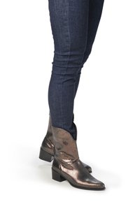 Metallisk bronsfärgade western-stil ankelskor med spetsig tå och låg klack, tillsammans med mörkblå slim fit-jeans.