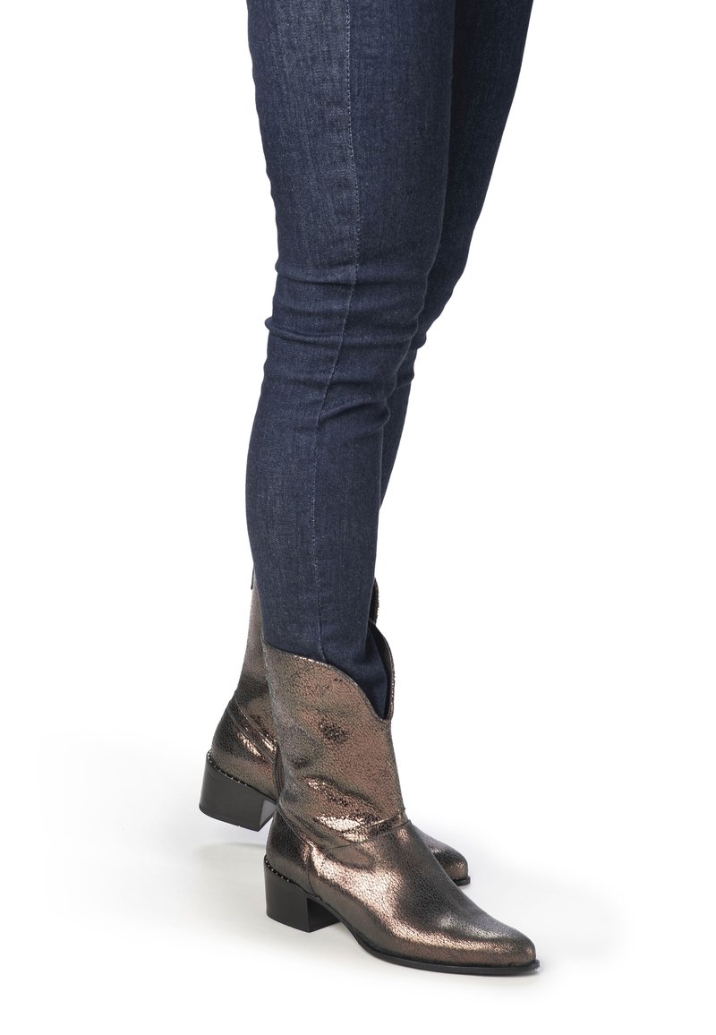 Metallisk bronsfärgade western-stil ankelskor med spetsig tå och låg klack, tillsammans med mörkblå slim fit-jeans.