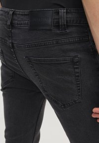 Jeans de mezclilla negra con un ajuste slim, que cuentan con un parche de cuero en la parte trasera de la cintura y un diseño de bolsillo trasero con ángulo distintivo.