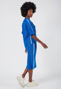 Blue, textured two-piece outfit with a loose-fitting top and knee-length skirt, featuring light blue side accents and paired with white sneakers.