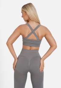 Grijze sportbeha met gekruiste banden, gecombineerd met hoge grijze leggings met textuuraccenten en een aansluitend ontwerp.