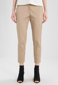 Beige anpassade byxor med en slät textur, avsmalnande bendesign och medelhög midja, tillsammans med svarta öppna tå ankle boots.