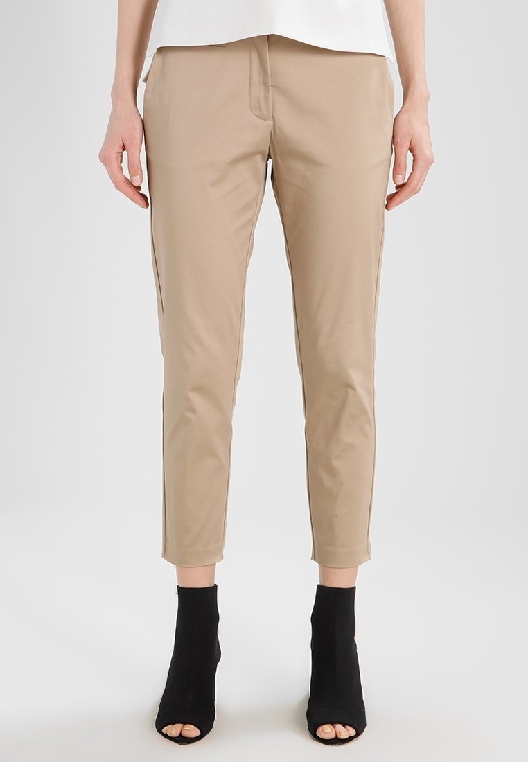 Beige anpassade byxor med en slät textur, avsmalnande bendesign och medelhög midja, tillsammans med svarta öppna tå ankle boots.