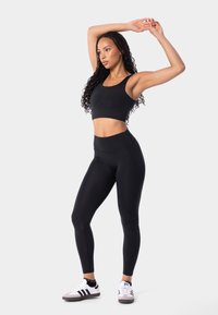 Černý sportovní crop top a legíny s vysokým pasem vyrobené z elastického materiálu, doplněné bílými a šedými teniskami se černými pruhy.