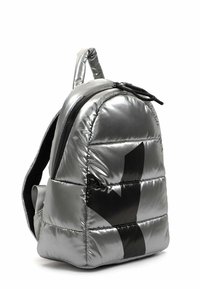 Sac à dos rembourré argenté avec une bande diagonale noire, fermeture éclair noire et poignée rembourrée, présenté légèrement incliné sur fond blanc.