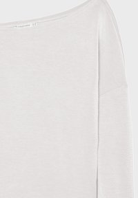 Chemise blanche à manches longues avec encolure bateau, coutures visibles et petite étiquette de marque au niveau du col.
