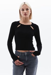 Top corto nero a maniche lunghe con dettagli a taglio sulle spalle e polsini arrotolati, abbinato a jeans grigi a vita alta.