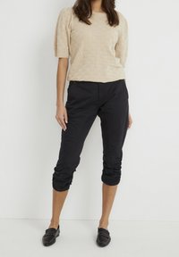 Beige texturerad stickad tröja med puffärmar, tillsammans med svarta capribyxor med rynkning vid fållen, bärs med svarta loafers.