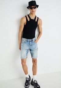 Top noir sans manches avec des détails découpés, shorts en denim bleu clair avec des ourlets retroussés, chapeau seau noir, lunettes de soleil foncées et baskets noires.