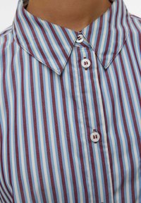 Camicia con colletto caratterizzata da righe verticali in azzurro chiaro e bordeaux, con chiusura a bottoni e in morbido tessuto di cotone.