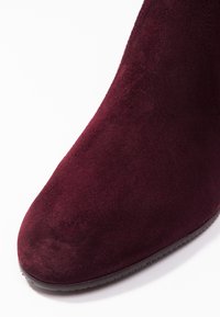 Bota de tobillo de ante burdeos con punta redondeada y acabado mate. La suela tiene una ligera textura con detalles mínimos.