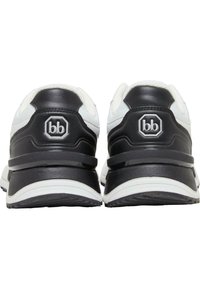 Svart-hvite joggesko med overdel i lær, avrundet tå, polstret krage og gummisåle med et hevet logo-akent på hælen.