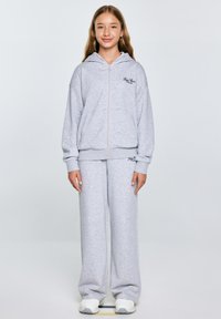 Siva zip-up kapuca s kapuco in logotipom na prsih, v kompletu z ujemajočimi se širokima trenirkama. Narejeno iz mehkega, strukturiranega blaga.