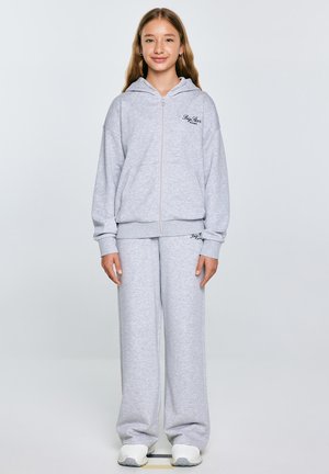 Haut à fermeture éclair gris avec capuche et logo sur la poitrine, associé à un pantalon de survêtement large assorti. Fabriqué en tissu doux et texturé.