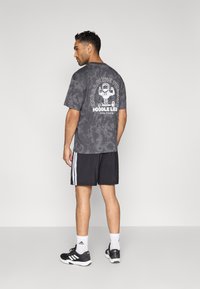 Hall halli tie-dye t-särk valge graafilise disainiga seljal, kombineeritud mustade lühikeste pükstega, millel on valged triibud, ja mustade spordijalatsitega.