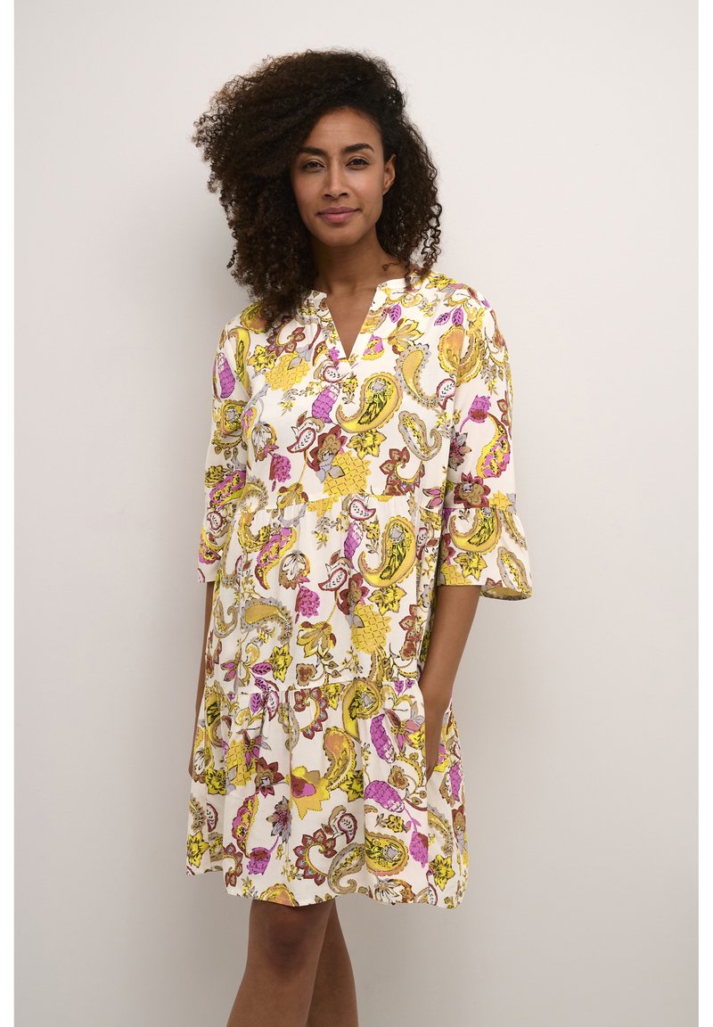 Abito bianco con motivo paisley in rosa, giallo e viola. Presenta un collo a V, maniche a tre quarti e tasche. Tessuto morbido e leggero.
