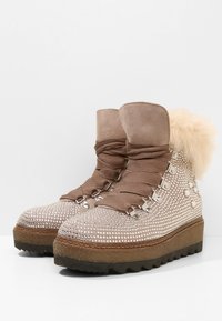 Botines beige con suelas de goma gruesa, tachuelas decorativas de plata, cordones anchos de tela y un borde de piel de pelo esponjoso en la parte trasera.