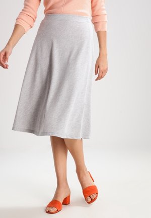Jupe midi A-line grise en tissu doux, avec une texture lisse. Associée à des sandales à talons blocs orange et un pull léger.