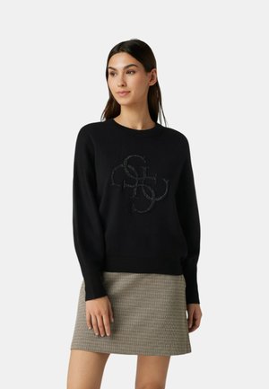 Maglione nero a maglia con maniche lunghe, polsini a coste e un design del logo strutturato. Abbinato a una gonna a scacchi in tonalità neutre.