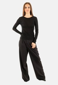 Top nero a maniche lunghe abbinato a pantaloni neri a vita alta e gamba larga, realizzati in tessuto morbido e con un fit rilassato.