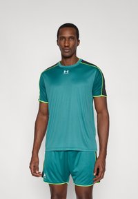 Türkizkék sportpóló fekete vállrésszel és neonzöld részletekkel, hozzáillő rövidnadrággal párosítva. Sima textúra, rövid ujjú, könnyű kialakítás.