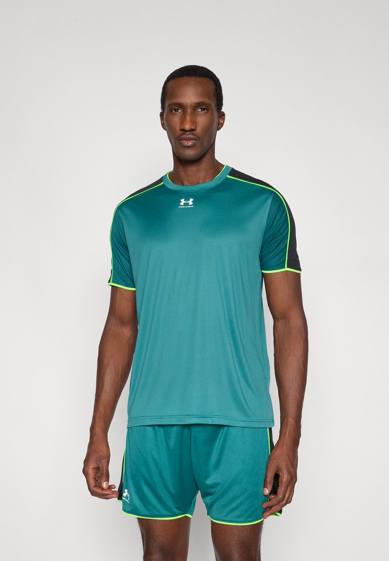 Türkizkék sportpóló fekete vállrésszel és neonzöld részletekkel, hozzáillő rövidnadrággal párosítva. Sima textúra, rövid ujjú, könnyű kialakítás.