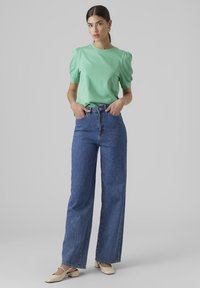 Mintgrön t-shirt med kort ärm och puffärm, kombinerad med högmidjade, vida blå denimjeans. Ljust färgade skor fulländar looken.