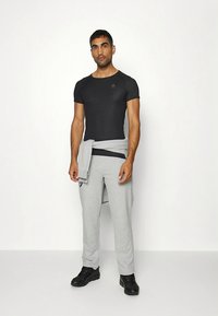 Svart figursydd T-shirt med korta ärmar, kombinerad med ljusgråa träningsbyxor och svarta sportskor. Tröja knuten avslappnat runt midjan.