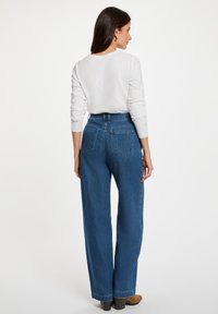 Vaqueros de tiro alto y pierna ancha en denim azul con una textura sutil. Presenta bolsillos traseros dobles y detalles de costura clásica.