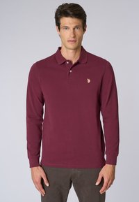 Polo a maniche lunghe color bordeaux con pattina a tre bottoni e un piccolo logo ricamato sul lato sinistro del petto. Tessuto in cotone liscio, vestibilità slim.