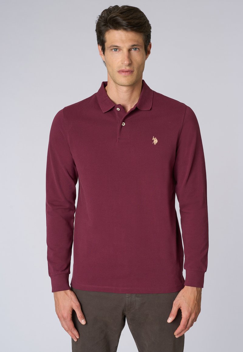 Polo a maniche lunghe color bordeaux con pattina a tre bottoni e un piccolo logo ricamato sul lato sinistro del petto. Tessuto in cotone liscio, vestibilità slim.