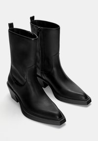 Botine negre din piele, cu vârf ascuțit, finisaj ușor texturat și toc mic pătrat. Au fermoar lateral și taburi pentru o mai bună prindere.