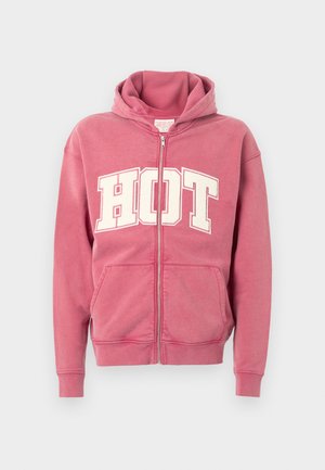 Roze zip-up hoodie met witte "HOT" letters aan de voorkant, voorzien van een capuchon met trekkoord en voorzakken. Zachte stof met een gladde textuur.