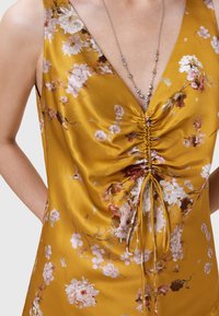 Abito in satin giallo senAPE con motivo floreale, dotato di scollo a V profondo e dettagli arricciati nella parte frontale, con un cordoncino in vita.