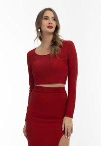 Punainen crop-top pitkähihaisilla, valmistettu kiiltävästä kankaasta. Yhdistetty vastaavaan hameeseen, jossa on korkeasaumainen halkio. Silkkinen pinta.