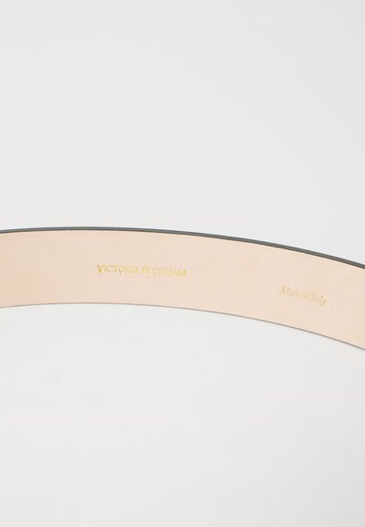 Curea din piele neagră cu o finisare netedă. Interiorul prezintă text în relief de aur: "VICTORIA BECKHAM" și "Fabricat în Italia".