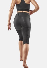 Schwarze Sportleggings mit einem Design bis zur Wade, ausgestattet mit strukturierten Einsätzen und einer Reißverschlusstasche am Bund. Glattes, dehnbares Material.