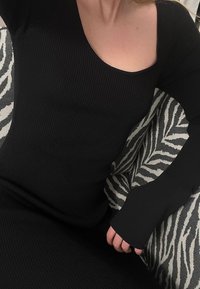Robe noire à manches longues côtelée avec un décolleté carré et une coupe ajustée. Un détail partiel à imprimé zèbre est visible sur le côté.