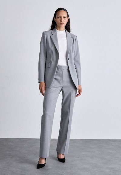 Blazer cinchado cinza com calças a condizer. Tecido suave, corte slim, lapelas com entalhe e padrão xadrez subtil. Finalizado com saltos altos pretos.
