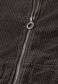 Silver zipper with round pull tab on dark brown corduroy fabric with vertical ridges.
