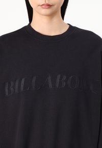 Fekete, kerek nyakú pulóver, hímzett "BILLABONG" logóval, azonos színű cérnával, puha, texturált anyagból készült.