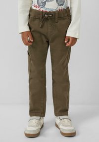 Kind wearing olijfgroene cargobroek met elastische tailleband en trekkoord, wit langom shirt en witte sneakers met grijze accenten.