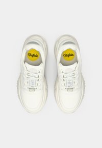 Adidași albi cu un design texturat, având o talpă stratificată, accente gri și un logo galben pe branț. Șireturile sunt afișate proeminent.