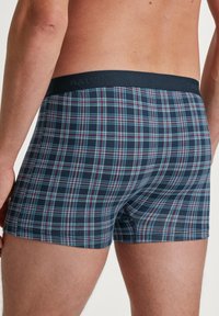 Marineblaue Karobermudashorts mit einem dunklen elastischen Bund, der mit Mustern aus hellblauen und roten Linien verziert ist. Weicher Stoff.