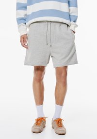 Shorts in cotone grigio con vita elastica e coulisse, caratterizzati da un orlo a taglio vivo e tasche laterali.