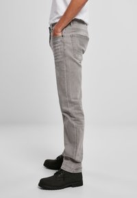 Jeans gris ajustados con un ligero desgaste, diseño de cinco bolsillos y detalles de costura sutil, combinados con botas negras de cordones.