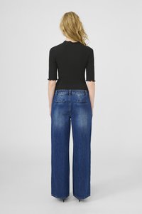 Melna ribota blūze ar īsām piedurknēm, apvienota ar augsto vidukli, platu zilo džinsu biksēm, kas satur divas aizmugures kabatas.