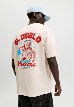 Homme de dos portant un t-shirt crème avec un graphisme rouge et bleu « El Diablo Taqueria Mexicana » représentant un lutteur masqué mangeant un taco.