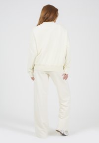 Lichtcrème kleurig loungewear set met een losse sweatshirt met geribde manchetten en bijpassende wijde broek. Zachte stoftextuur.